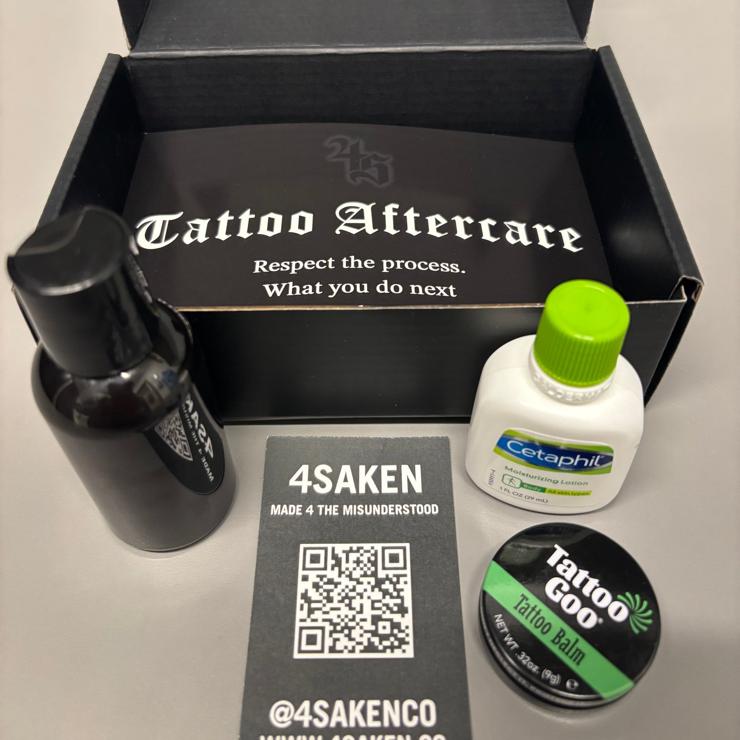 Tattoo aftercare product set with bottle, applicator, and packaging on a gray surface.